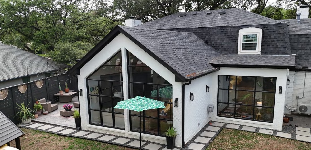 Modern home with black roof, white exterior, and a glass sunroom addition overlooking a patio.